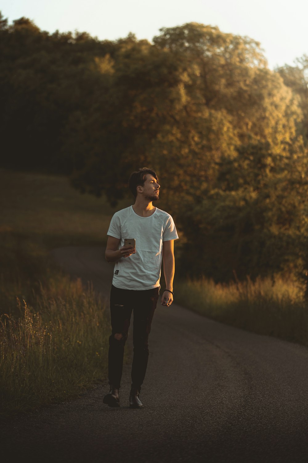 man in white crew neck t-shirt and black pants standing on road during daytime