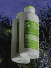 Two bottles of Simple Kind to Skin Replenishing Rich Moisturizer are shown, with water droplets on the surface, set against a dark, wet background.
