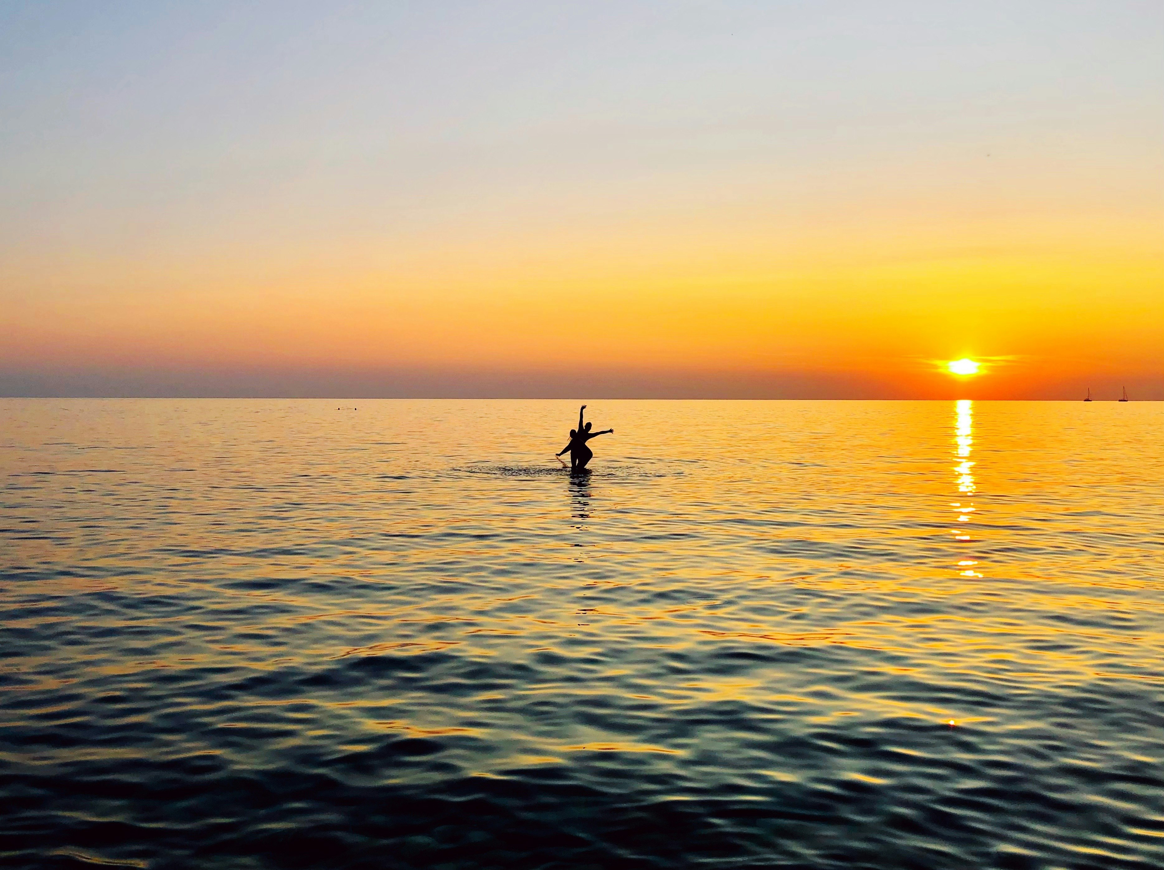 silhouette of 2 people on body of water during sunset