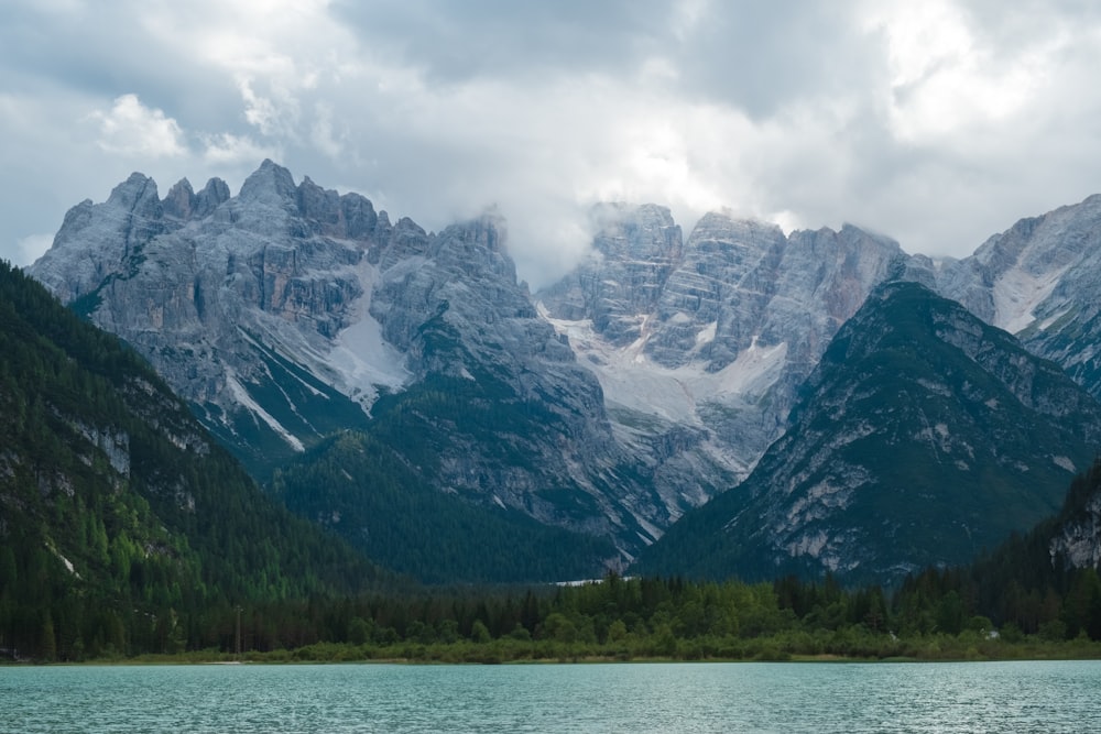 green trees near body of water and mountain under white clouds during daytime