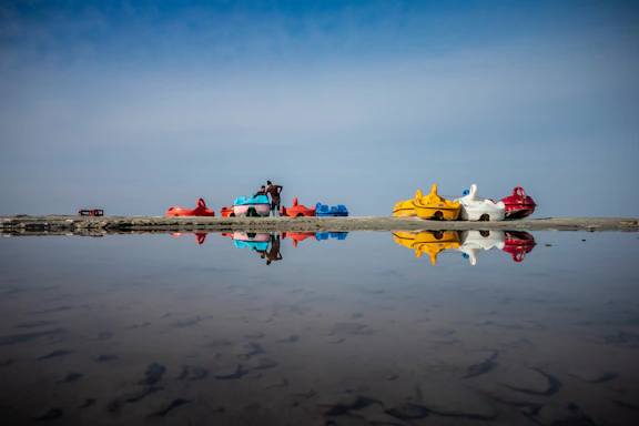 A serene view of the waterkart base with paddleboards and pedalos lined up by the turquoise water under a clear sky.