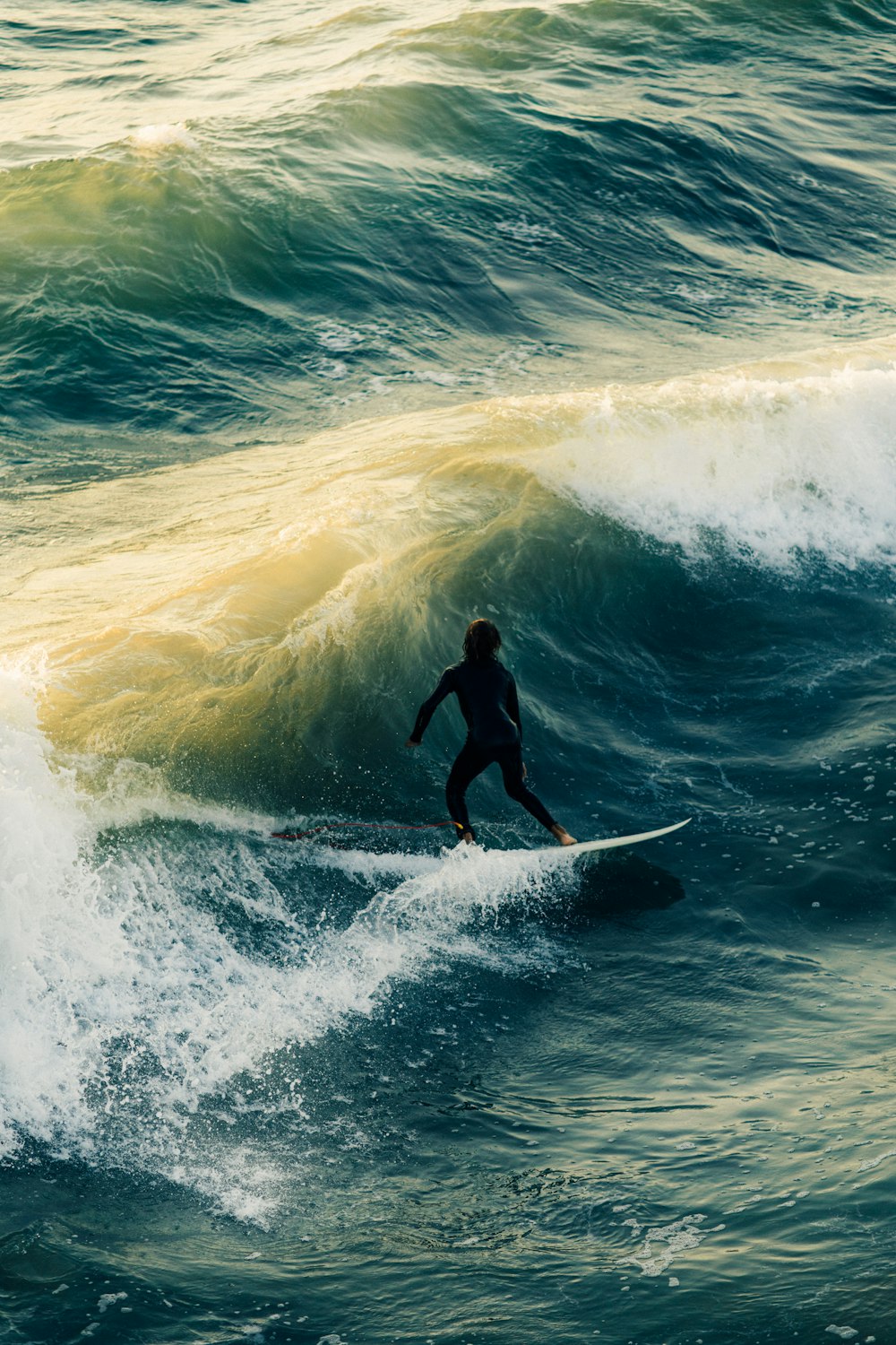 uomo in muta nera che fa surf sulle onde del mare durante il giorno