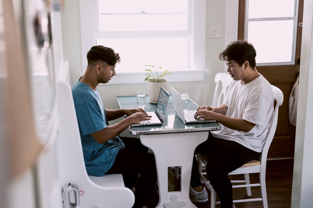 2 boys sitting on chair using laptop computers
