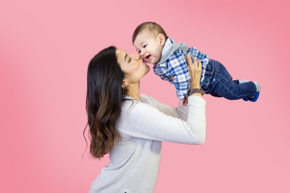 donna in camicia bianca a maniche lunghe che trasporta il bambino in camicia a quadri blu e bianca