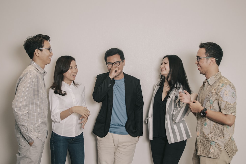 3 women and 2 men standing beside white wall