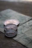 Three coins are placed on top of a paper currency with intricate designs. The focus is on the coins, which appear to have an embossed profile of a person and include engraved text.