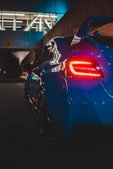 A sleek luxury electric car parked in a modern urban setting at night with neon blue lighting.