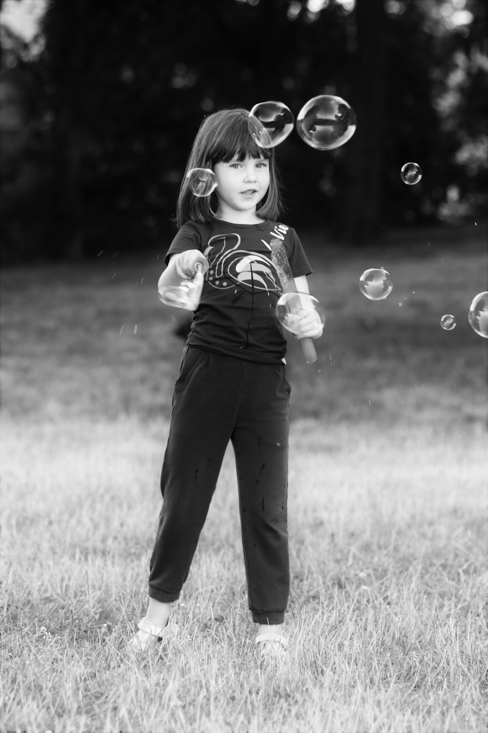 girl in white and pink shirt and black pants standing on grass field with bubbles in in in in in