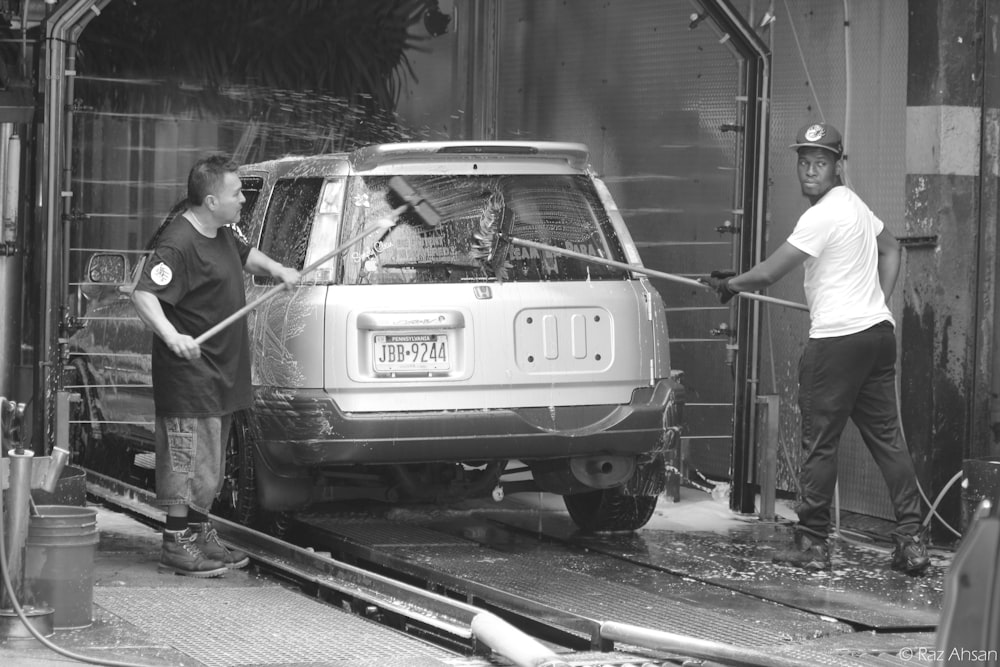 grayscale photo of man standing beside white car