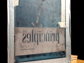 An image of a mirror reflecting reversed text that reads 'principles.' The frame appears rustic with noticeable wear and tear, with a blue tint and some taped edges.