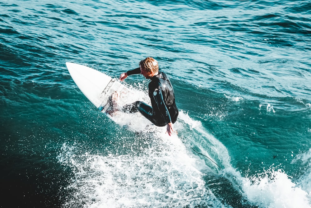 man in black wet suit riding white surfboard on sea waves during daytime