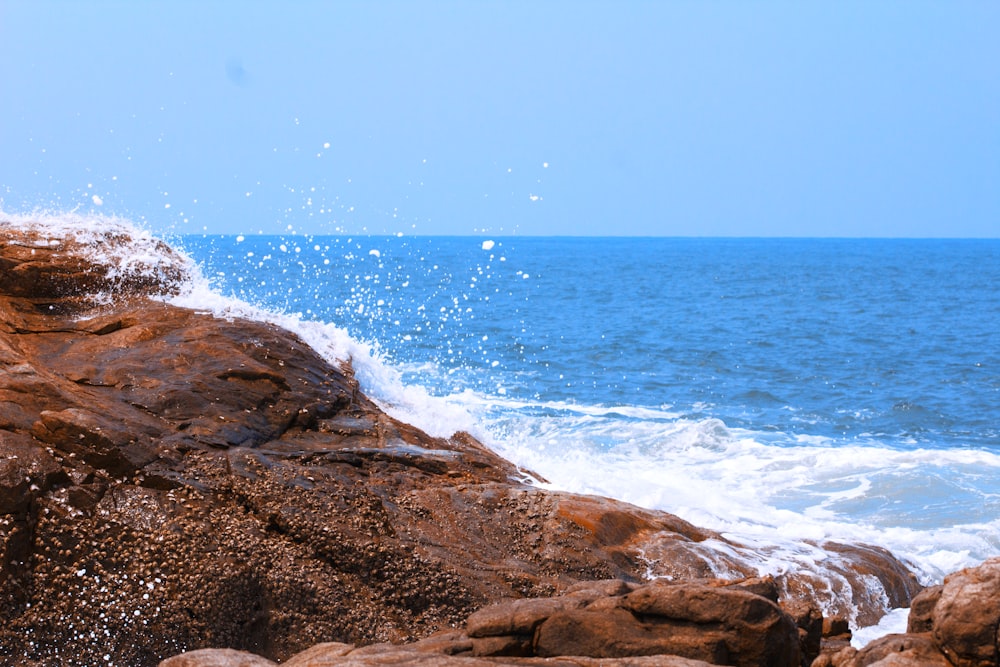 ocean waves crashing on brown rocky shore during daytime