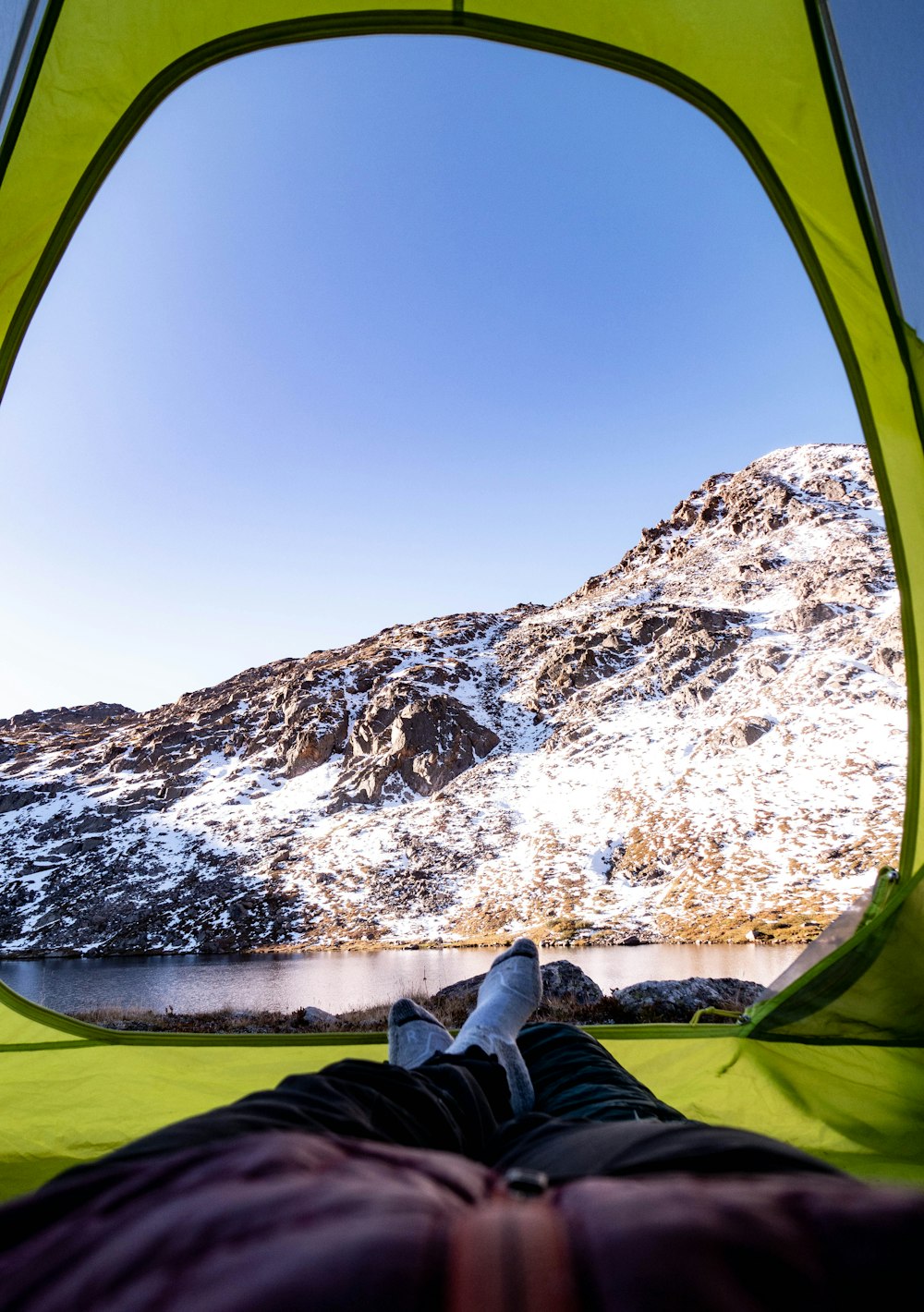 person in black pants sitting inside tent looking at snow covered mountains during daytime