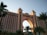 A large, luxurious hotel with a grand arch at its center, flanked by two towers featuring numerous windows. The building is surrounded by lush palm trees and bathed in soft sunlight, suggesting a location likely in a coastal or tropical region.