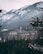 A large, historic hotel with a Canadian flag is nestled among snow-covered trees and mountainous terrain. The hotel features a classic architectural style with numerous windows and gabled roofs, set against a backdrop of rugged, snow-dusted mountains.