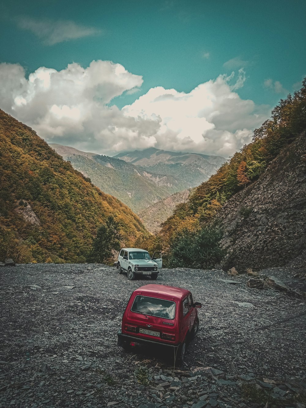 white and red suv on gray asphalt road near green mountains under blue and white sunny