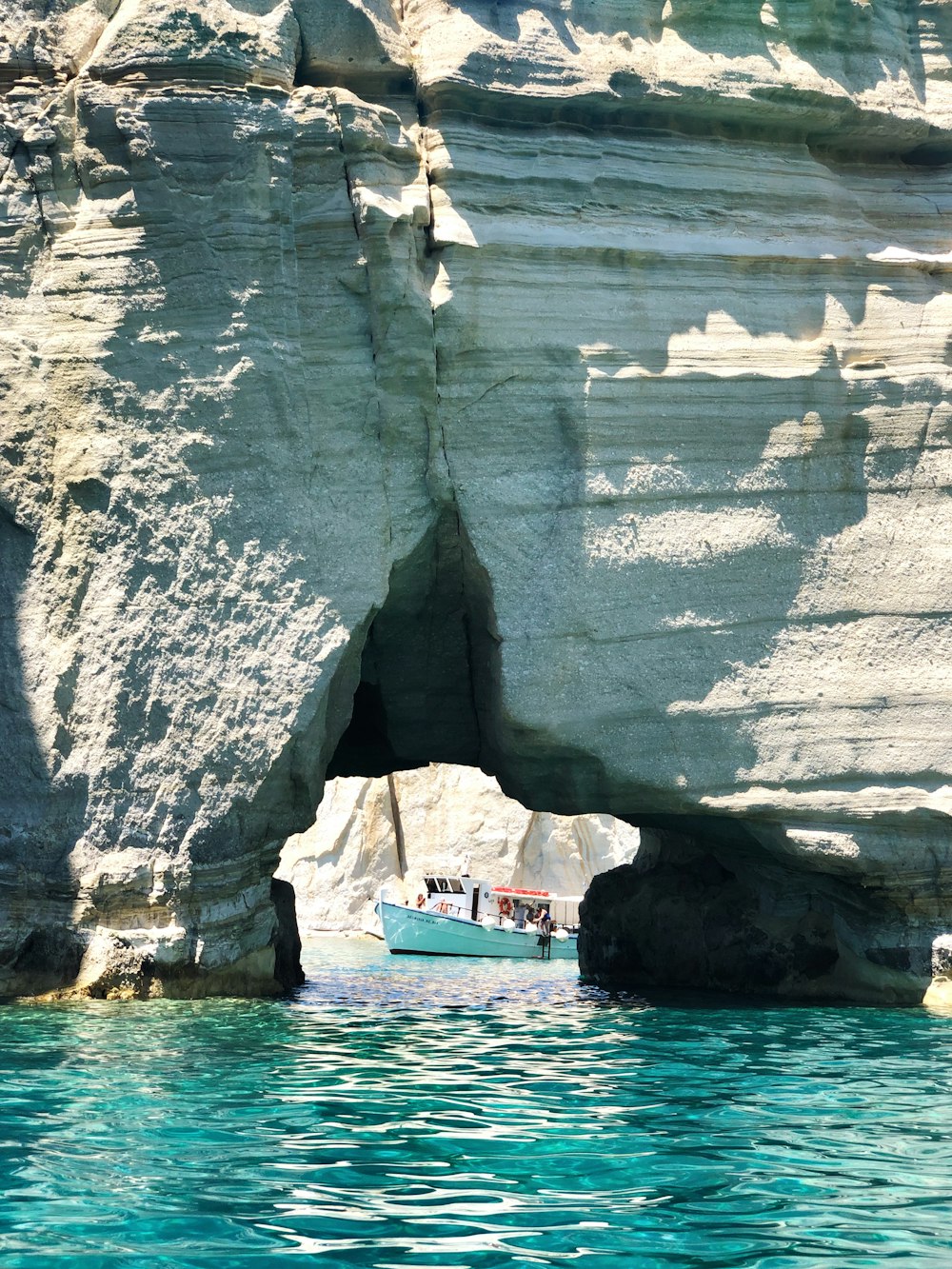 weißes Boot auf See in der Nähe von Felsformationen während des Tages