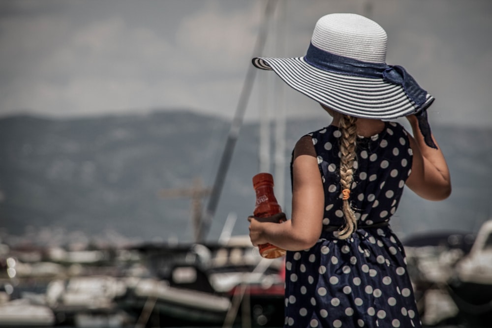 Femme en robe à pois bleu et blanc et chapeau de soleil blanc tenant une bouteille rouge