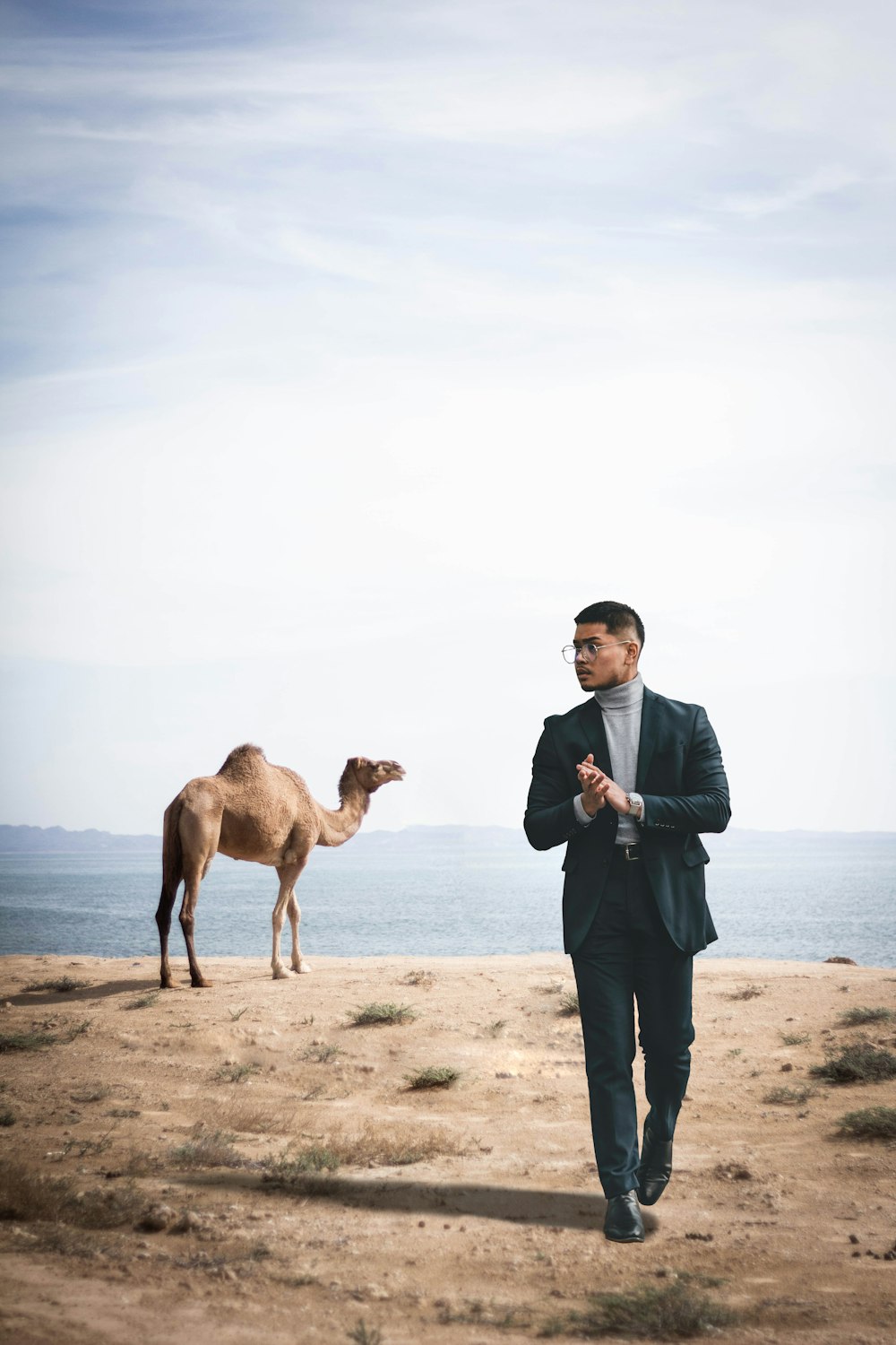 uomo in camicia blu e pantaloni neri in piedi accanto al cammello marrone durante il giorno