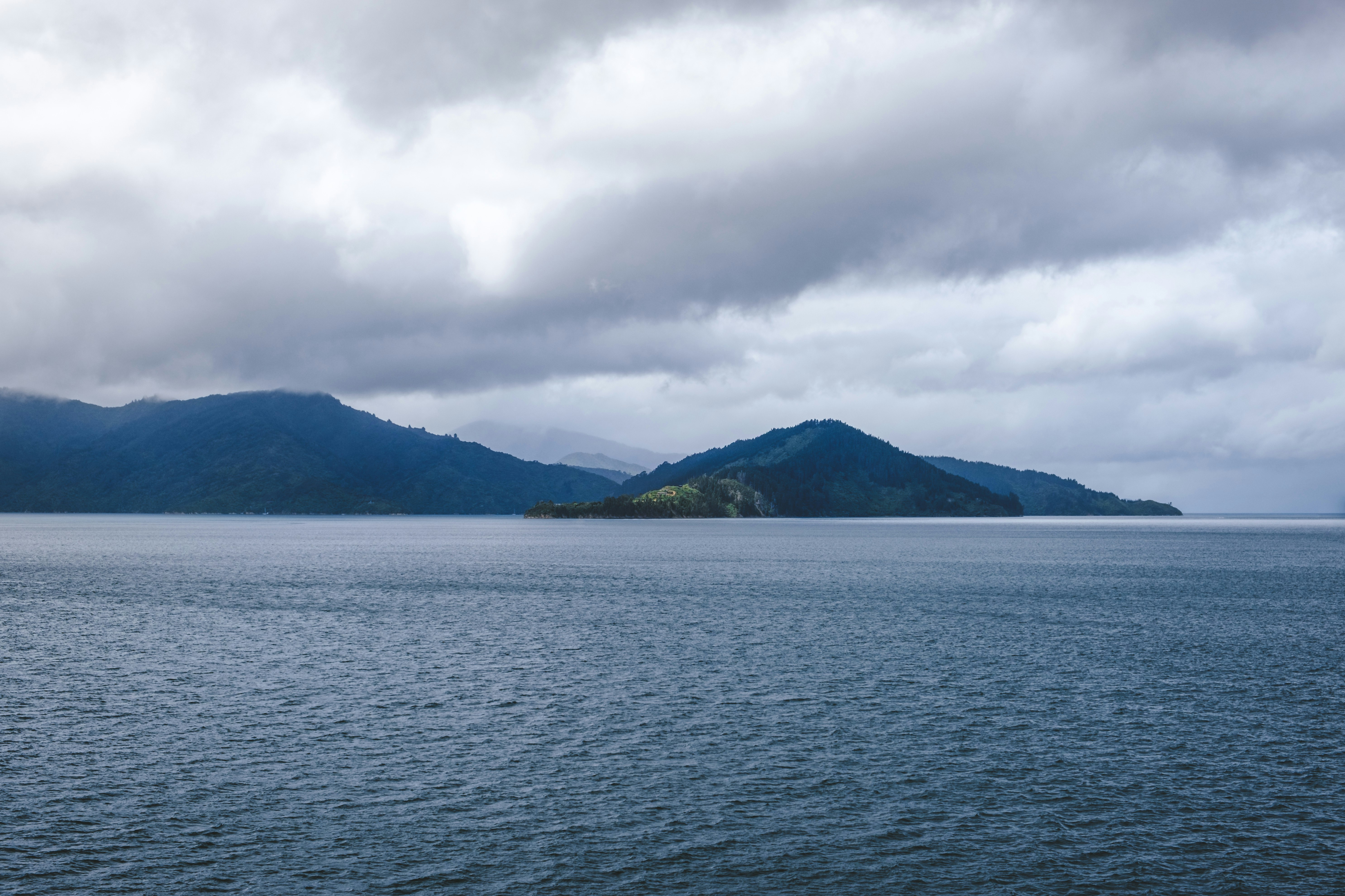 body of water near mountain under cloudy sky during daytime