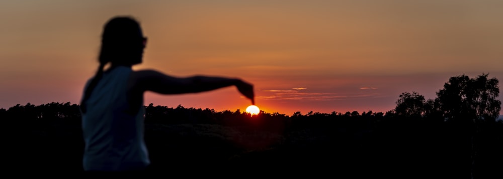 silhouette of person raising right hand during sunset