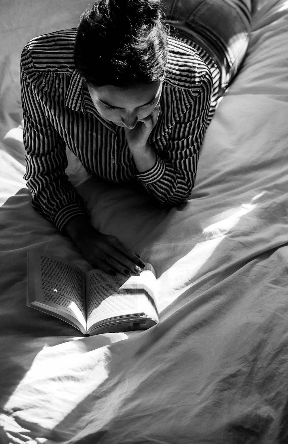 grayscale photo of man reading book on bed