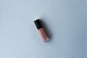 Close-up of a shimmering nude gloss tube placed elegantly on soft pastel fabric.