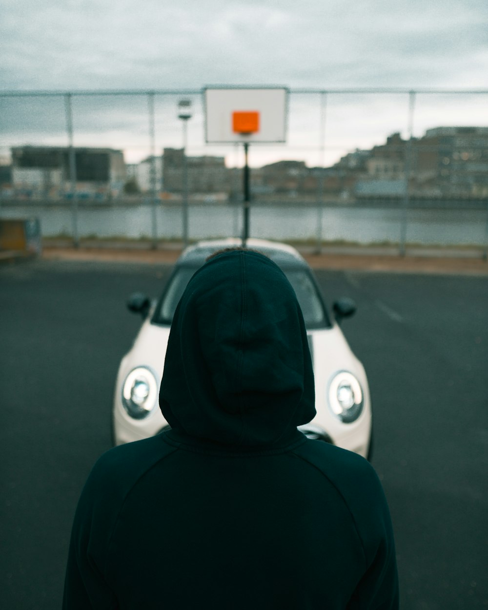 a person in a hoodie standing in front of a car