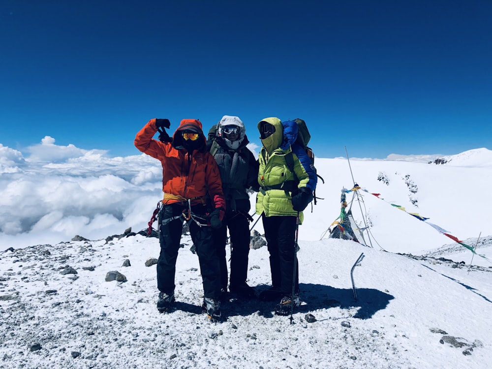 3 person in green jacket and black pants standing on snow covered ground during daytime