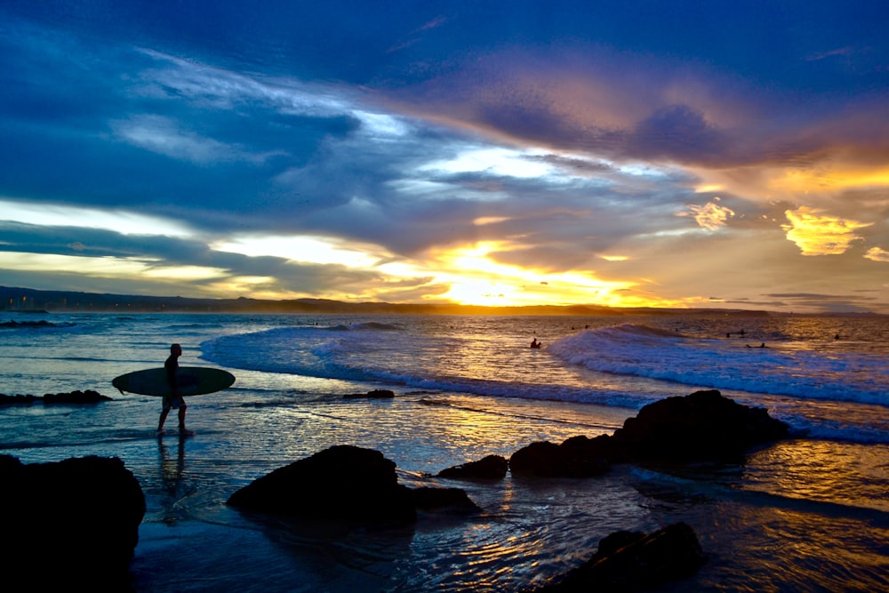 silhouette of 2 people standing on seashore during sunset