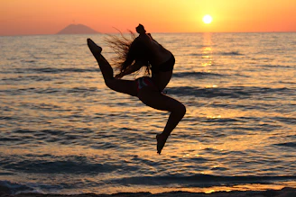 woman in black tank top and black shorts jumping on beach during sunset