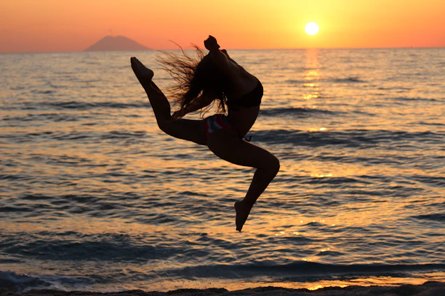woman in black tank top and black shorts jumping on beach during sunset