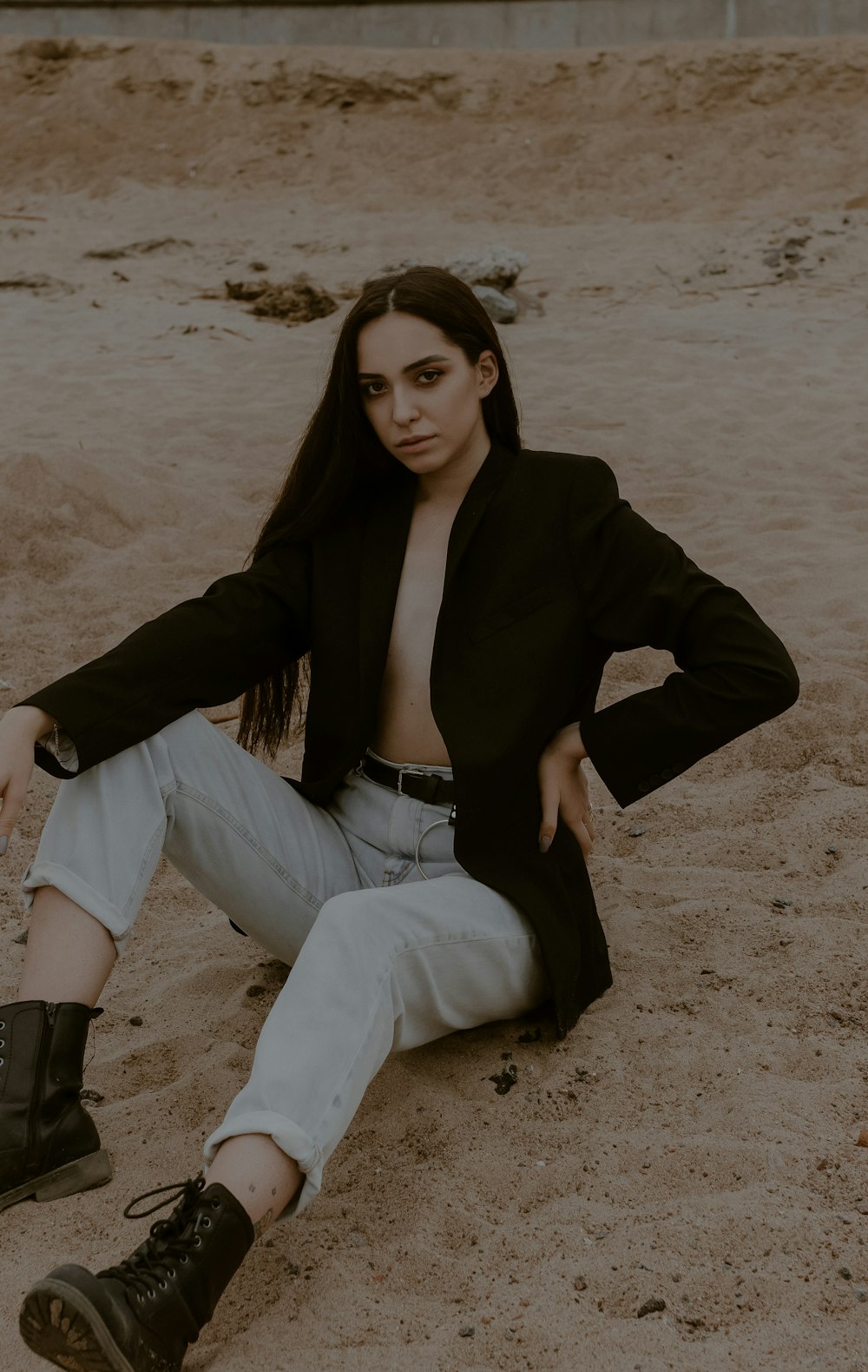 woman in black blazer and white pants sitting on brown sand during daytime