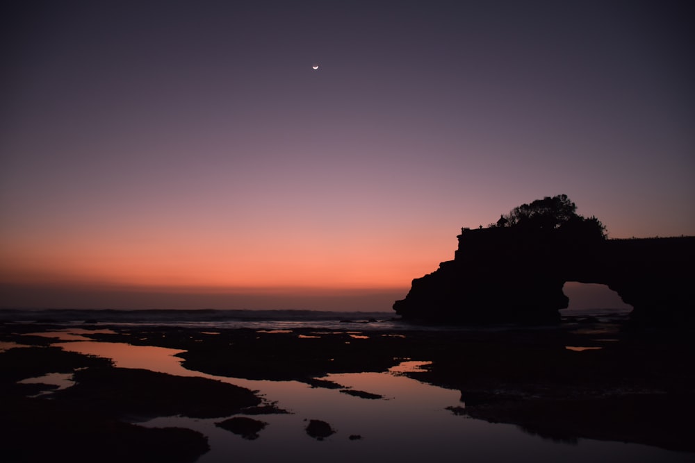 silhouette of mountain near body of water during sunset