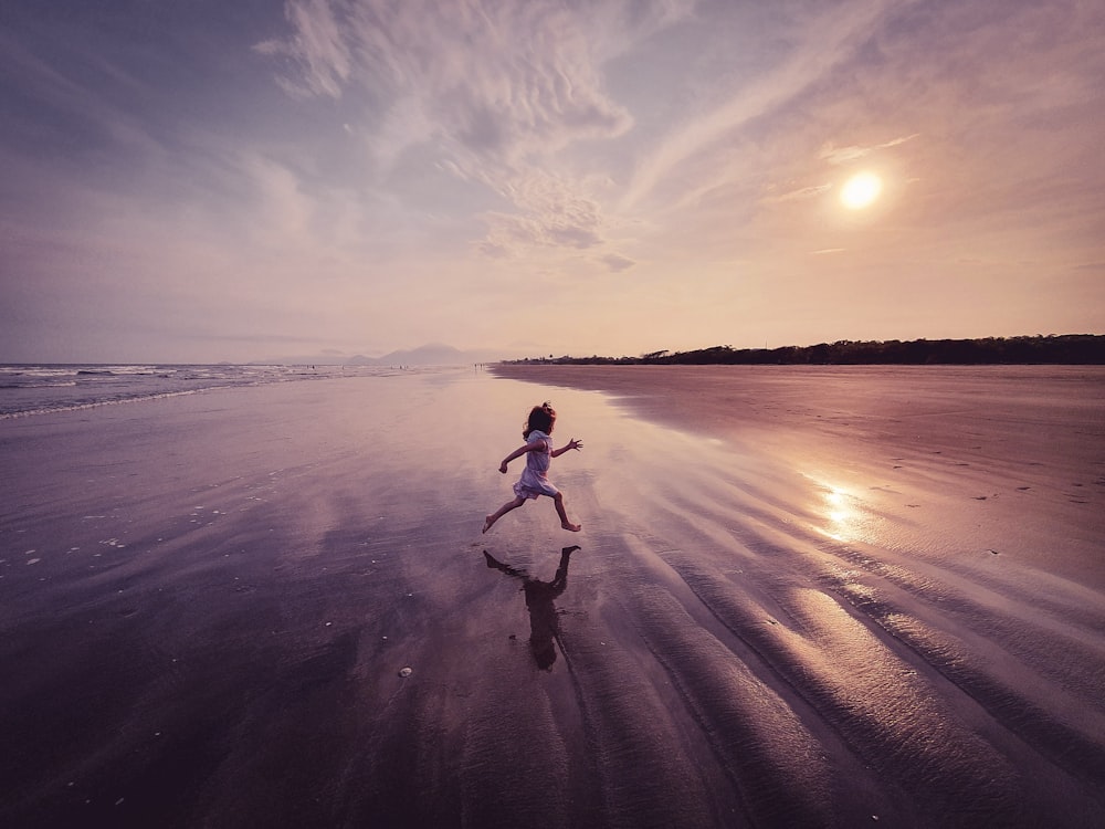 woman in white tank top and black pants running on beach during sunset
