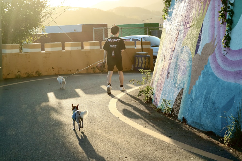 man in black t-shirt and gray shorts walking with white dog during daytime