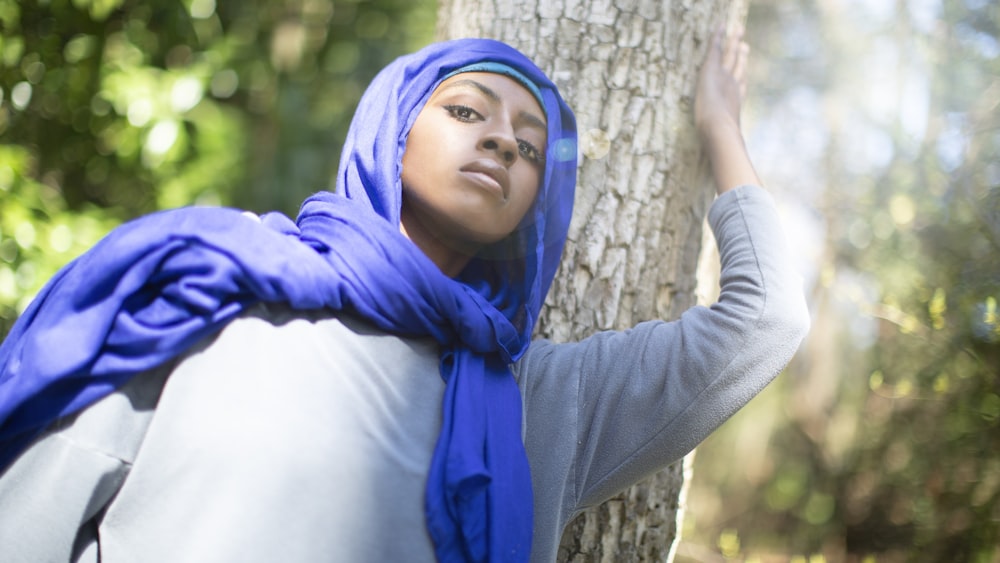 갈색 나무 줄기에 기대어 있는 파란 히잡을 쓴 여자