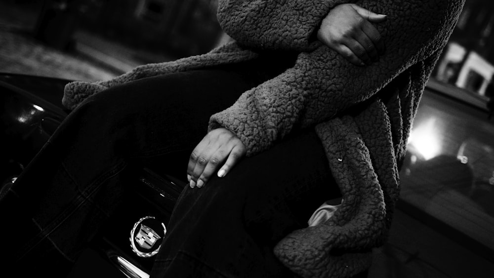 Persona con chaqueta negra y pantalones grises sentada en un asiento de automóvil negro