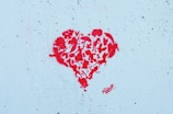 A graffiti-style red heart composed of various animal silhouettes and abstract shapes stands out against a textured light blue background.