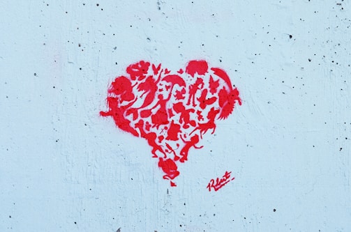 A graffiti-style red heart composed of various animal silhouettes and abstract shapes stands out against a textured light blue background.