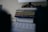 A stack of colorful notebooks rests on top of a white electronic device with a perforated front panel featuring a 'G' logo. The scene is dimly lit, creating an intimate and cozy atmosphere in an indoor setting.