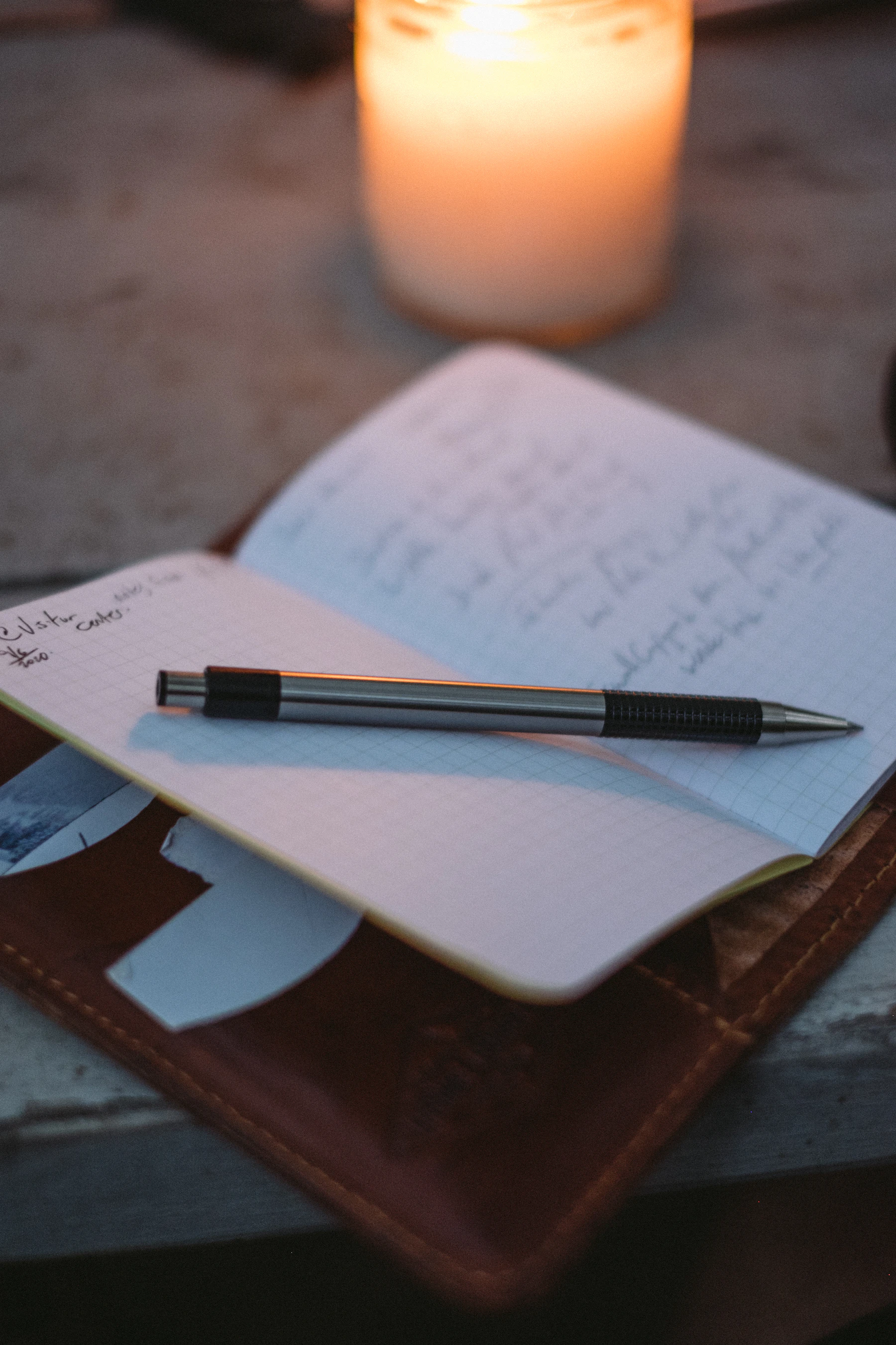 A small open notebook of handwritten notes with a pen lying across it, a lit candle behind