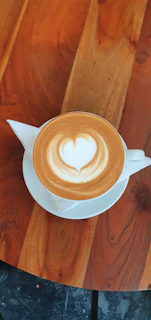 A warm latte art heart on a creamy coffee surface inside a rustic ceramic cup, set on a blush linen napkin with soft natural light.