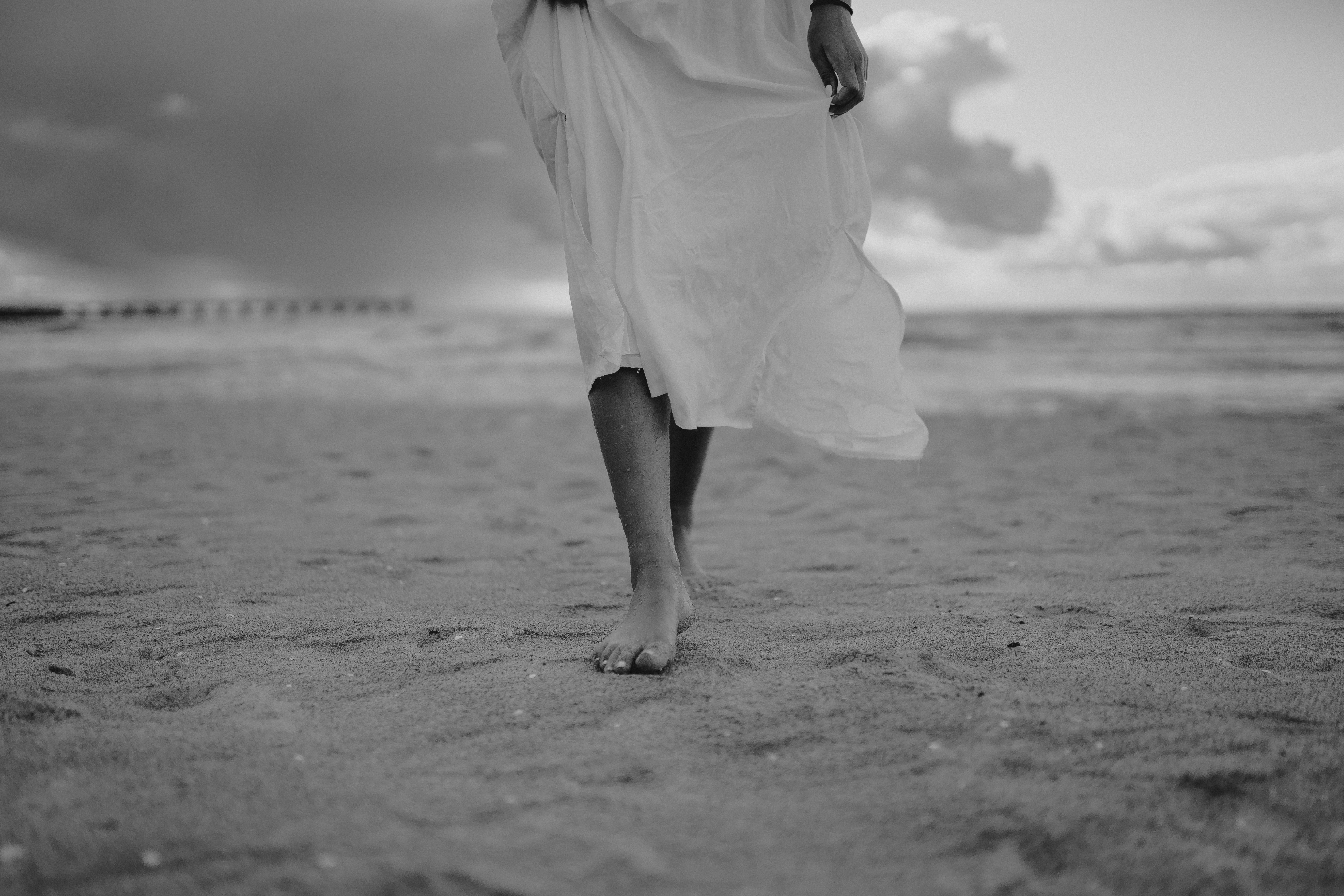 grayscale photo of woman in dress walking on beach