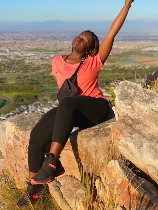 woman in orange shirt and black pants sitting on rock during daytime in Ou Kaapse Road South Africa