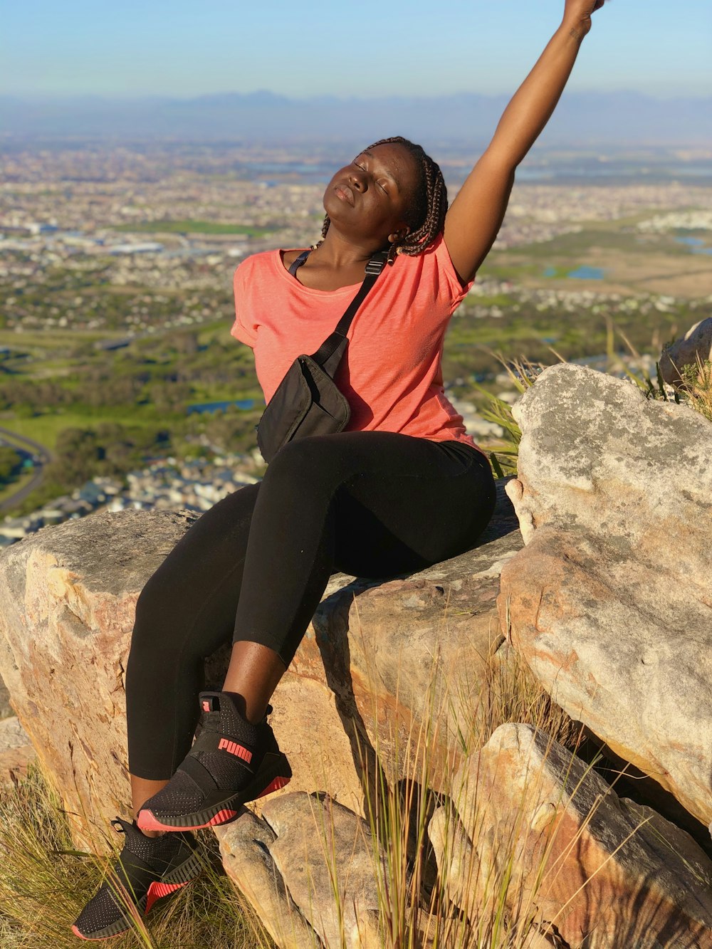 woman in orange shirt and black pants sitting on rock during daytime