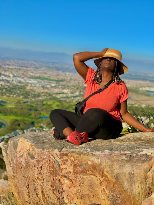 woman in black tank top and black pants sitting on brown rock during daytime in Ou Kaapse Road South Africa