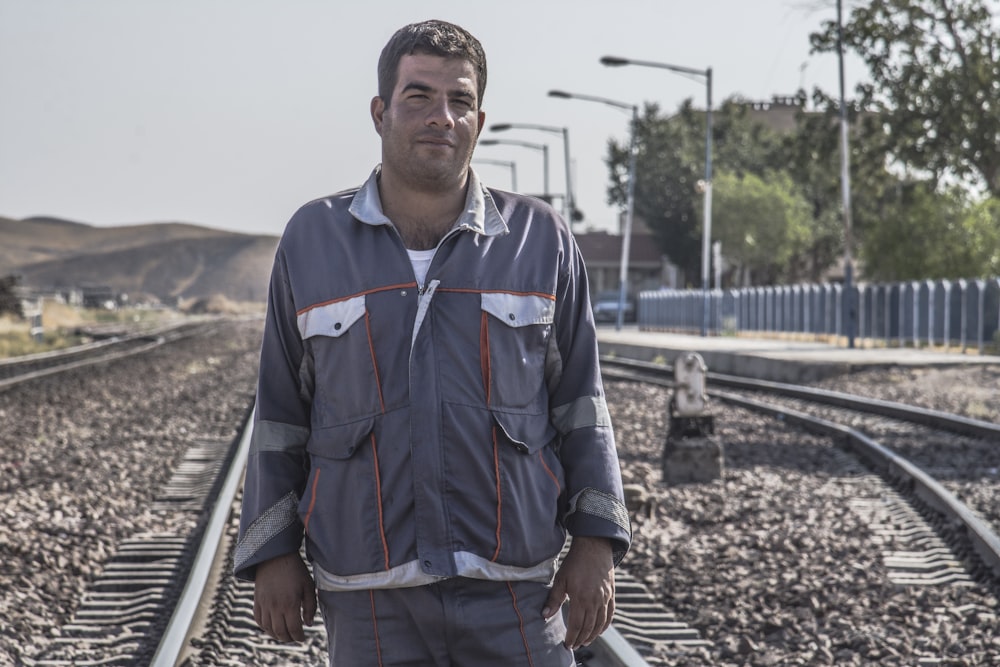 man in blue and red button up shirt standing on train rail during daytime