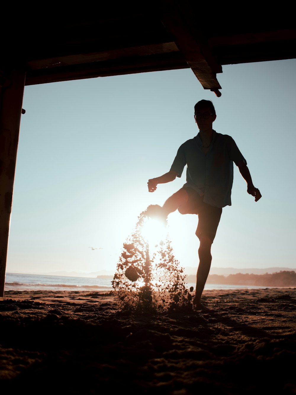 man in black t-shirt and shorts standing on beach shore during sunset