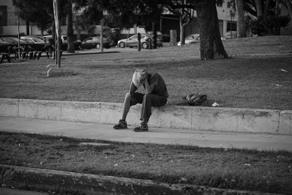uomo in t-shirt e pantaloni seduto sul pavimento di cemento nella fotografia in scala di grigi